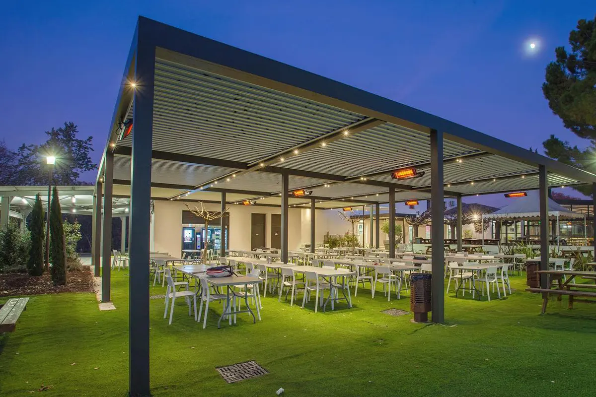 Otwarty ogródek gastronomiczny pod pergolą z promiennikami HEATSCOPE nad stolikami